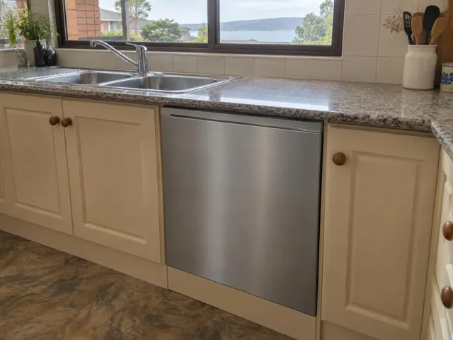 Integrated dishwasher under a stone kitchen benchtop beside a double sink and cream cabinetry in Warners Bay