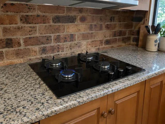 Black gas cooktop set into a speckled stone kitchen benchtop with brick splashback in Macquarie Hills